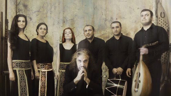 A group of 7 people in black outfits, standing shoulder to shoulder. 